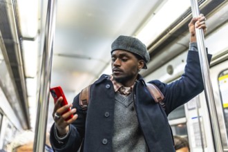 African american man on subway train holding a pole and browsing his smartphone during a commuting