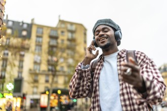 Young man in a beret and headphones smiling and dancing while walking through a vibrant urban