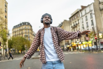 Young black man with headphones and backpack enjoying music and dancing freely with arms