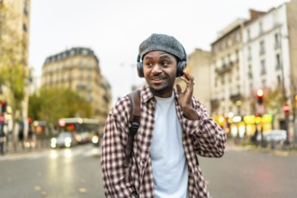 Young black man enjoying music through headphones while walking on an urban street, adjusting his