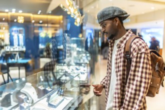 Young black man wearing a plaid shirt and cap intently looking at a display case filled with