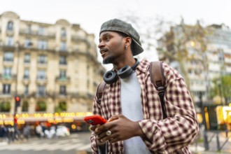 Young man using a smartphone and wearing headphones, a backpack, and a casual plaid shirt while