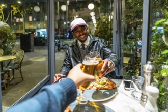 Young man smiling and feeling happy while toasting beer glasses with a friend during an evening