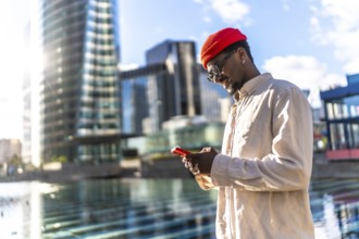 Young black man smiling while interacting with a smartphone outdoors, surrounded by modern city