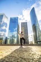 Black man striking a dynamic pose while dancing outdoors in a modern commercial district with glass