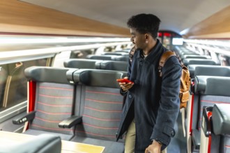 Young male passenger in a modern train carriage looking for his seat while checking travel