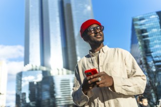 Young black man wearing a red beanie and glasses, smiling and looking up while holding a red