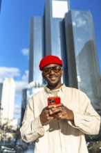 Stylish young black man wearing a red beanie and sunglasses, holding a bright red smartphone and