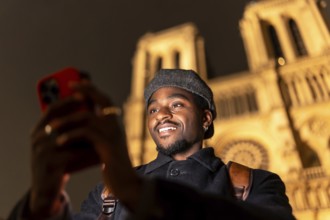 Young man enjoying a night street experience in paris, france, holding a smartphone and smiling