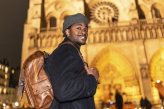 Young black man smiling while wearing a beret and backpack, standing in front of the illuminated