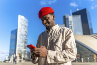 Young african american man smiling while typing on his smartphone outdoors in a sunny high tech