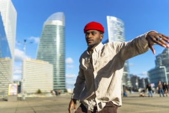Black man wearing a red beanie and casual clothing moving rhythmically on a sunny day in an urban