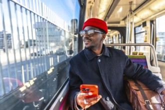 African man passenger traveling by tram, looking out the window while holding a mobile phone,