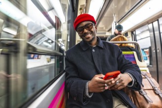 Young man smiling directly at the camera while holding and using a red smartphone, sitting on a