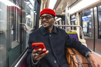 Young smiling african american man in a stylish coat and red beanie sits on a city train, holding a