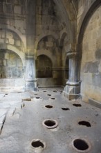 Stone room with large floor holes and massive pillars surrounded by weathered walls, Haghpat