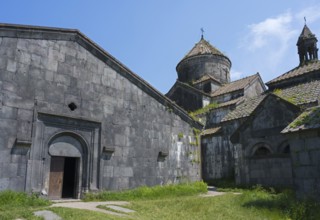 Massive stone church with large windows and an open wooden gate under a blue sky, Haghpat
