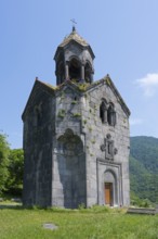 Small stone church with bell tower, surrounded by green nature and high-altitude mountains in the