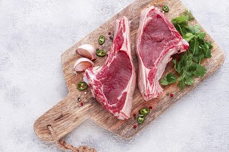 Fresh pieces of beef on the bone, on a wooden cutting board, with herbs and spices, ready for