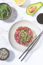 Fresh tuna tartare with avocado served on a marble table with soy sauce and seaweed salad