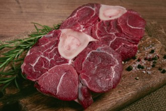 Knuckle on the bone, raw meat for ossobuco, on a wooden chopping board, with a sprig of rosemary,