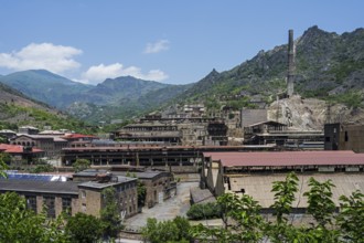Industrial plant in a mountainous area with old buildings and chimney surrounded by green hills,