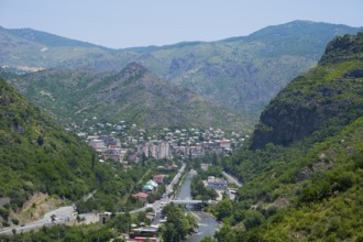 Mountain landscape with a town in the valley surrounded by lush greenery and a river flowing