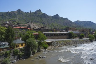 Industrial building on the riverbank surrounded by mountains and green trees, former copper