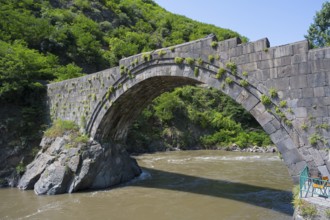 Historic stone bridge with vegetation spanning arches, river flowing below, Sanahin bridge across