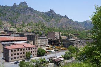 Industrial buildings nestled in a mountainous landscape under bright blue sky, former copper