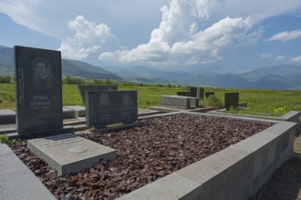 Tombstones in a cemetery with mountain landscape and blue sky in the background, grave decorated