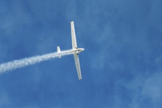 Stunt aerobatic plane performing stunts in blue sky with smoke trail. Concept of speed, difficulty,