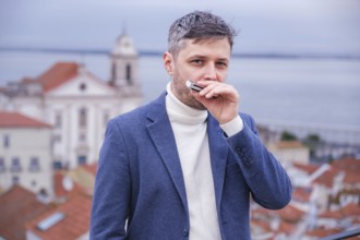 Man musician in a blue blazer and white sweater playing blues on a harmonica with eyes closed,