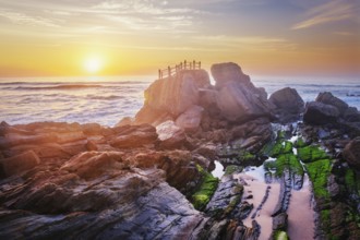 Scenic rock formation at Praia da Santa Cruz, Portugal, with ocean waves and vibrant sunset sky