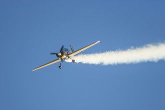 Golden stunt aerobatic plane performing stunts in blue sky with smoke trail. Concept of speed,