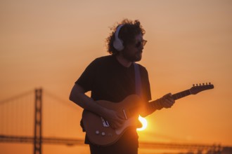 Hipster street musician in black playing electric guitar in street outdoors on sunset