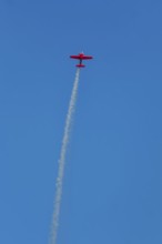 Red stunt aerobatic plane performing stunts in blue sky. Concept of speed, difficulty, precision,