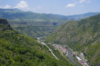 A valley with a river and a small town nestled in green mountains under blue skies, views of