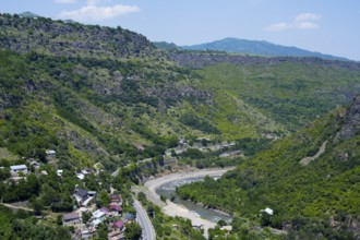 A valley with a river surrounded by wooded mountains and scattered houses under blue skies, views