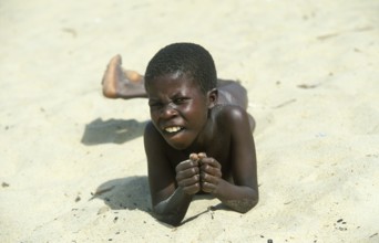 Local boy lying in the sand at Kande Beach on Lake Malawi and smiling at the camera, Malawi,