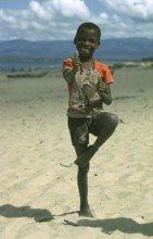 A cheerful local boy with a ripped shirt stands on the beach near Kande Beach on Lake Malawi and