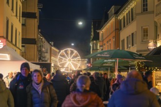A Ferris wheel in the distance illuminates a busy street of a Christmas market, Christmas market
