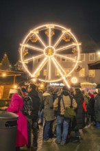 People gather in a Christmas square in front of an illuminated Ferris wheel, Christmas market 2025,