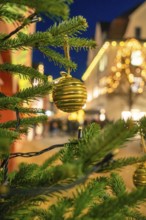 Festive photo of a golden Christmas ball on pine branches with light decoration at night, Christmas