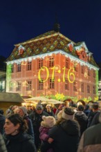 Colourfully illuminated building with time projection on a busy Christmas market at night,