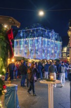 Illuminated building with Christmas projections in front of numerous market visitors, Christmas