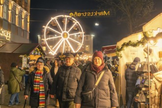 People stroll through an illuminated market with a large Ferris wheel in the background, Christmas