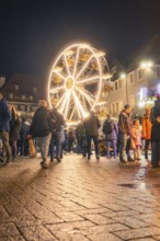 People walk across a square with illuminated Ferris wheel at night, Christmas market 2025, Nagold,
