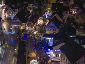 Aerial view of a Christmas market at night with a dense crowd and illuminated half-timbered houses,
