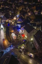 Aerial view of an illuminated Christmas market at night with a shiny Christmas tree and crowds of